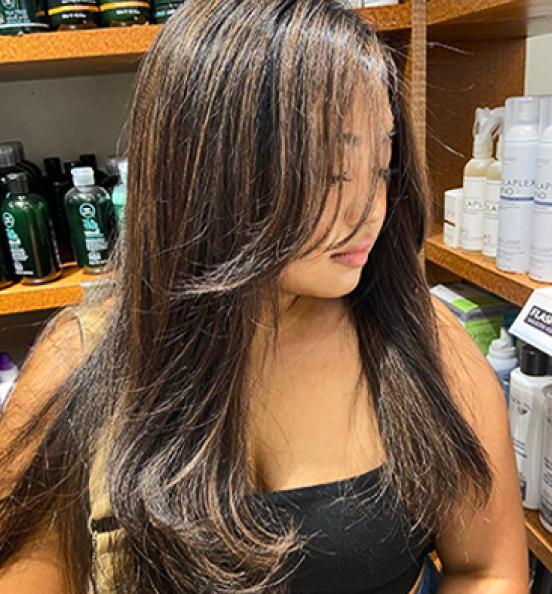 Woman with long, highlighted hair stands in front of shelves with beauty products. Image links to Hair Cuttery's Instagram account.